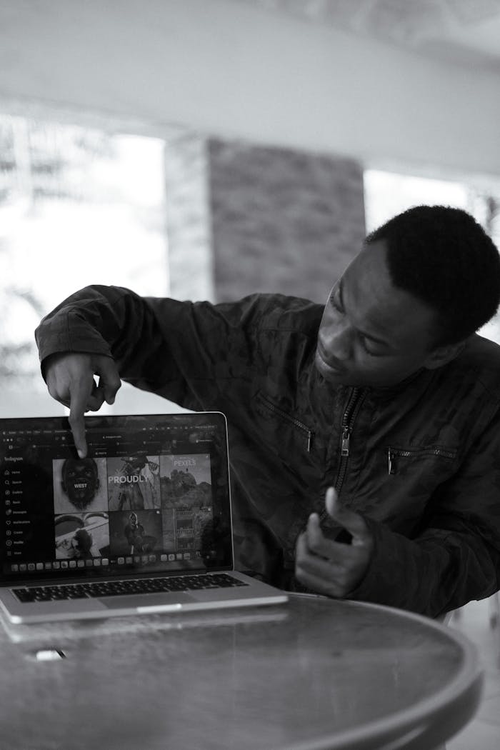 Black and white photo of a man pointing to a laptop screen indoors in Nigeria.